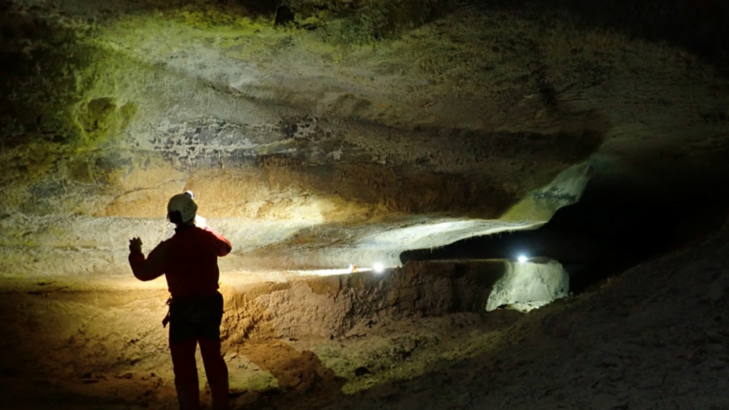 A person stands in a dark cave holding a flashlight.
