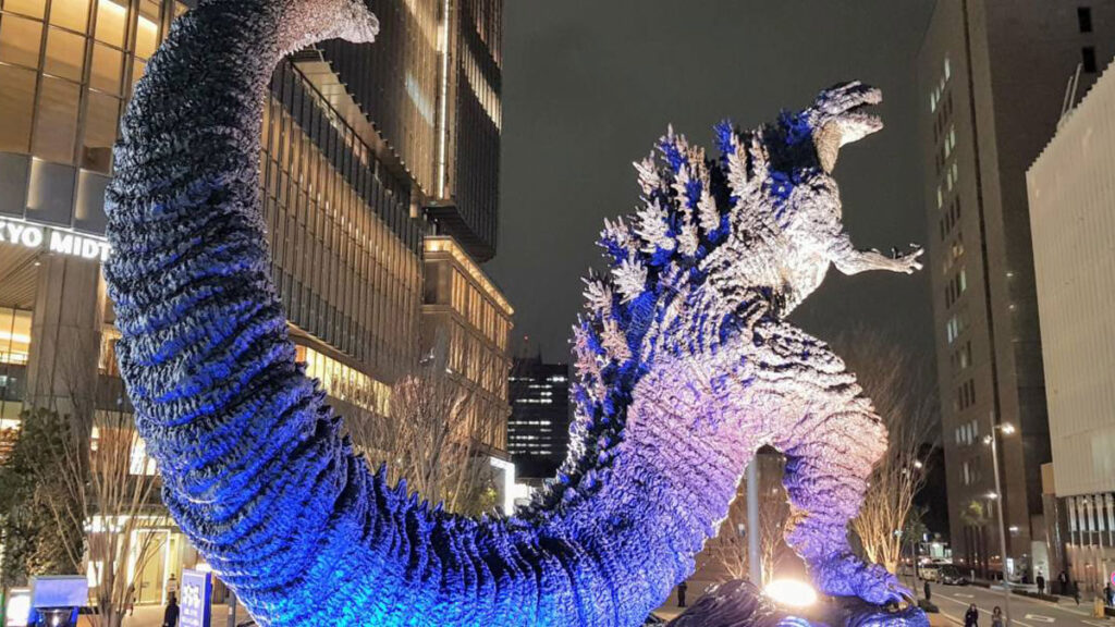 A photo of a statue of a dinosaur-like creature next to city buildings.