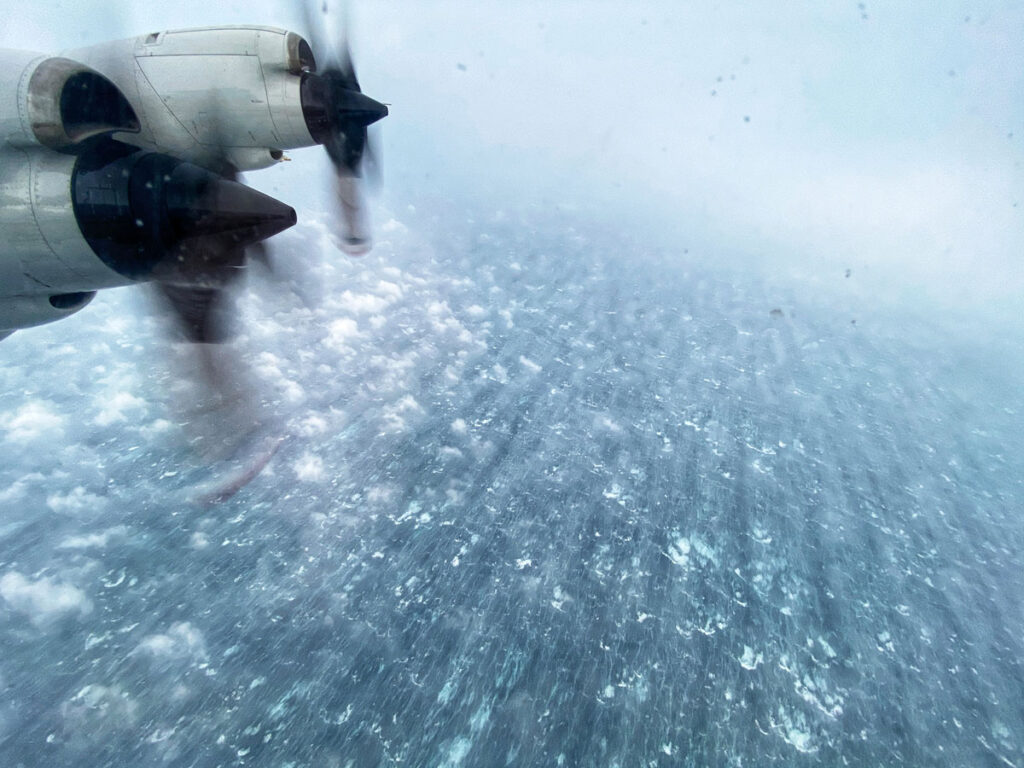 A photo out an airplane window of two propellers and rough seas.