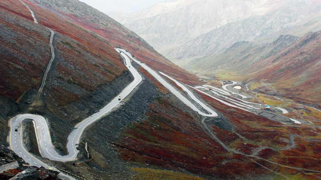 A road winds through a mountain landscape covered in red mossy vegetation and shrubs.