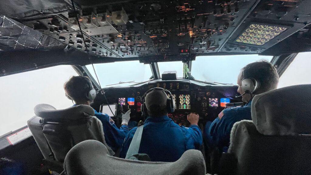 Photo of the cockpit of an aircraft and three people sitting in a row facing the front window.