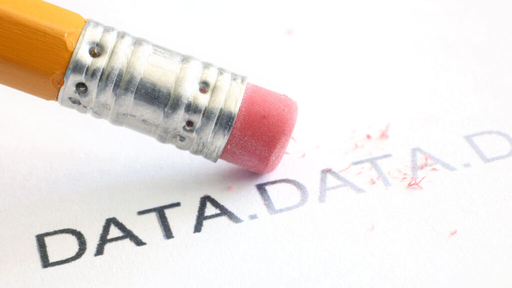 Close-up view of a pencil eraser erasing the word “DATA” on a piece of white paper.