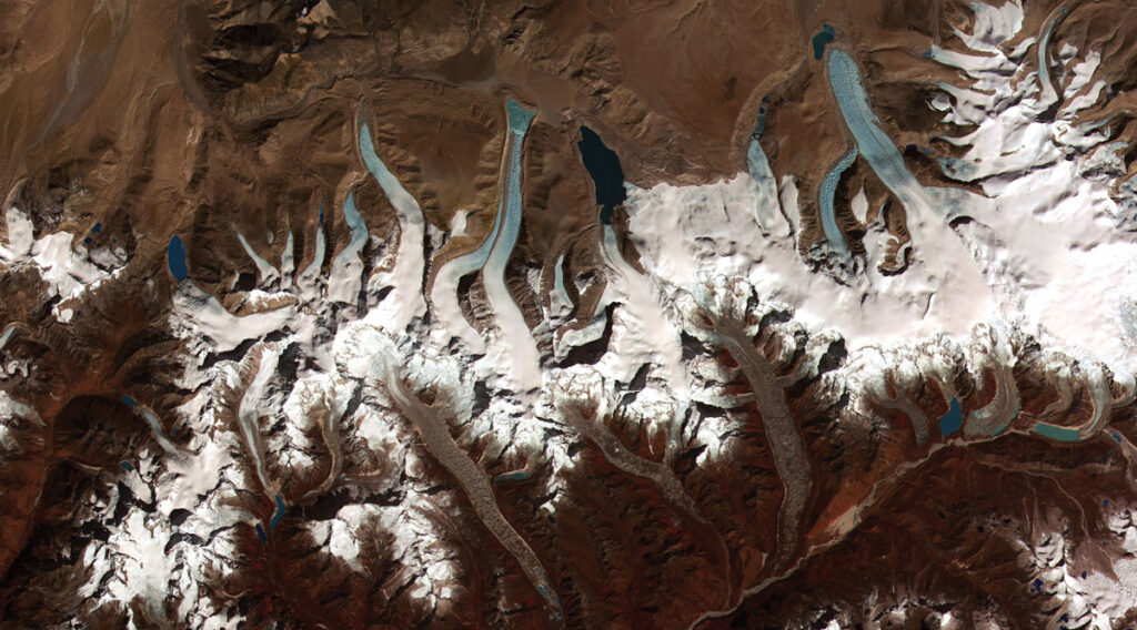 Fingers of white ice end in blue lakes against a brown background in this view of glaciers in Bhutan.
