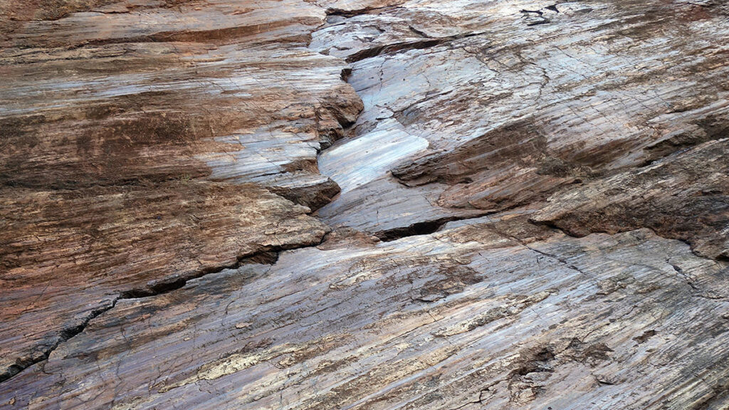 A tan and brown striped rock surface with a fault running through the middle