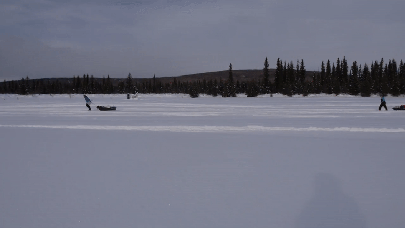 Three people tow sleds across a snow-covered lake.