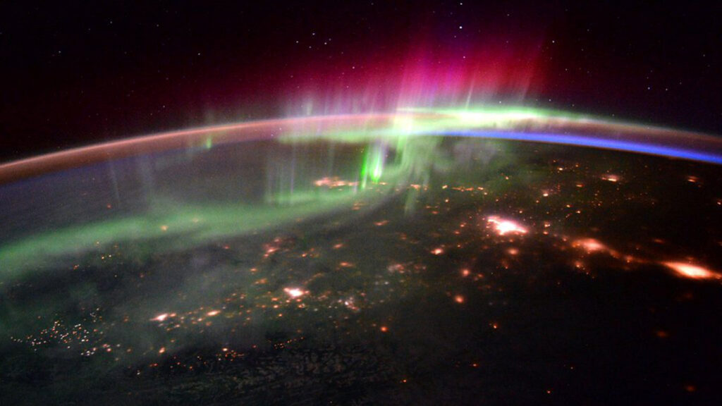 Photo looking down on Earth from a satellite, showing red and green streaks flickering in the atmosphere