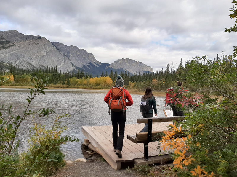 Photo of a lake with mountains in the background. People are walking in front of the lake facing away from the camera.
