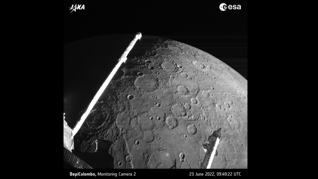 A photo of a cratered, gray sphere. Two long arms of a spacecraft are visible in the foreground.
