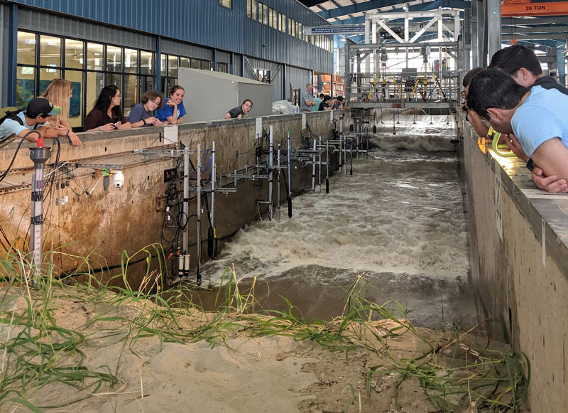 Una foto de un canal de concreto con arena y agua. Hay gente viendo sobre las orillas del canal