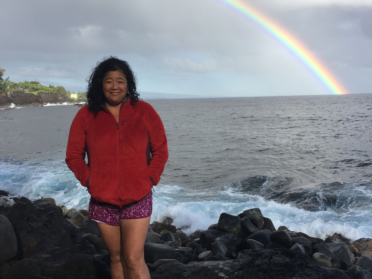 Photo of a person looking at the camera while standing on rocks by a water body.