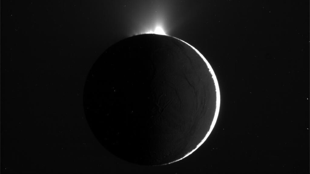 Sunlight shines through plumes of ice crystals and dust grains jetting from a gray sphere.