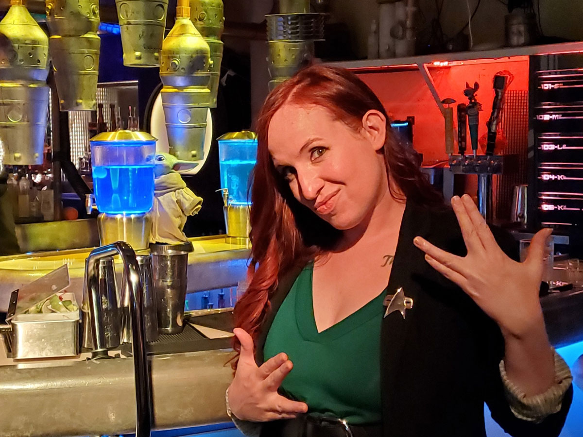 Erin Macdonald makes a Vulcan salute (a hand sign of greeting from Star Trek) at a bar while wearing a Star Trek badge.