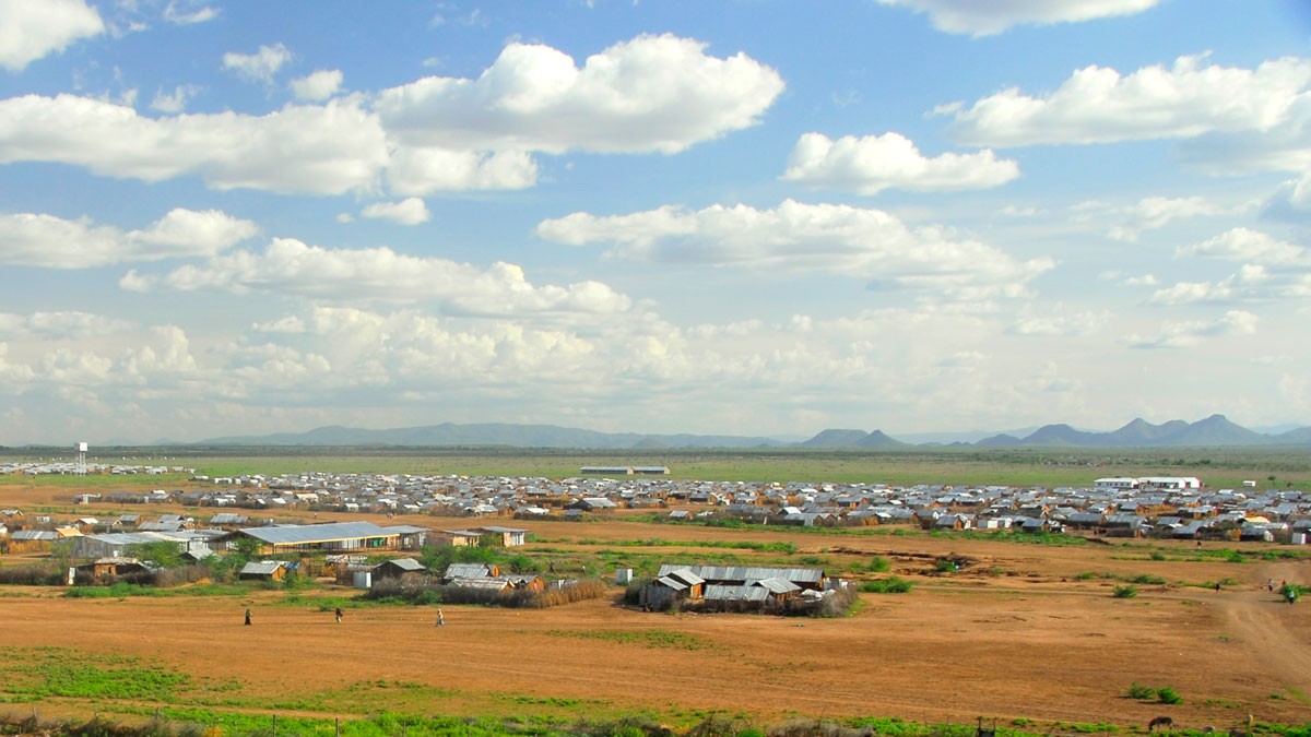 Photo of a flat brown and green landscape with gray metal single-story structures scattered throughout.