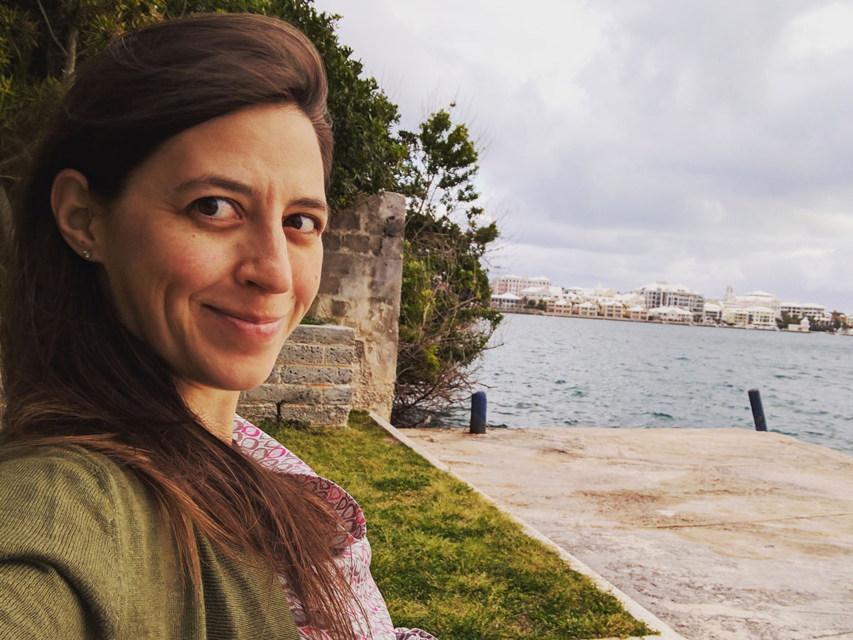 A woman smiles at the camera while sitting next to a body of water.