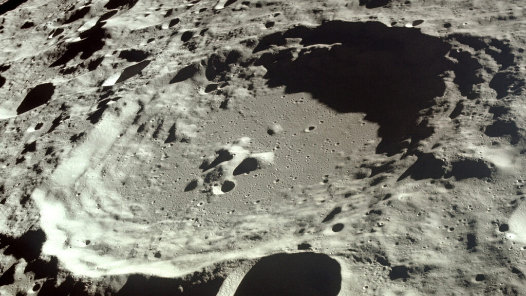 A close-up image of the Moon showing a single large crater surrounded by a field of smaller craters