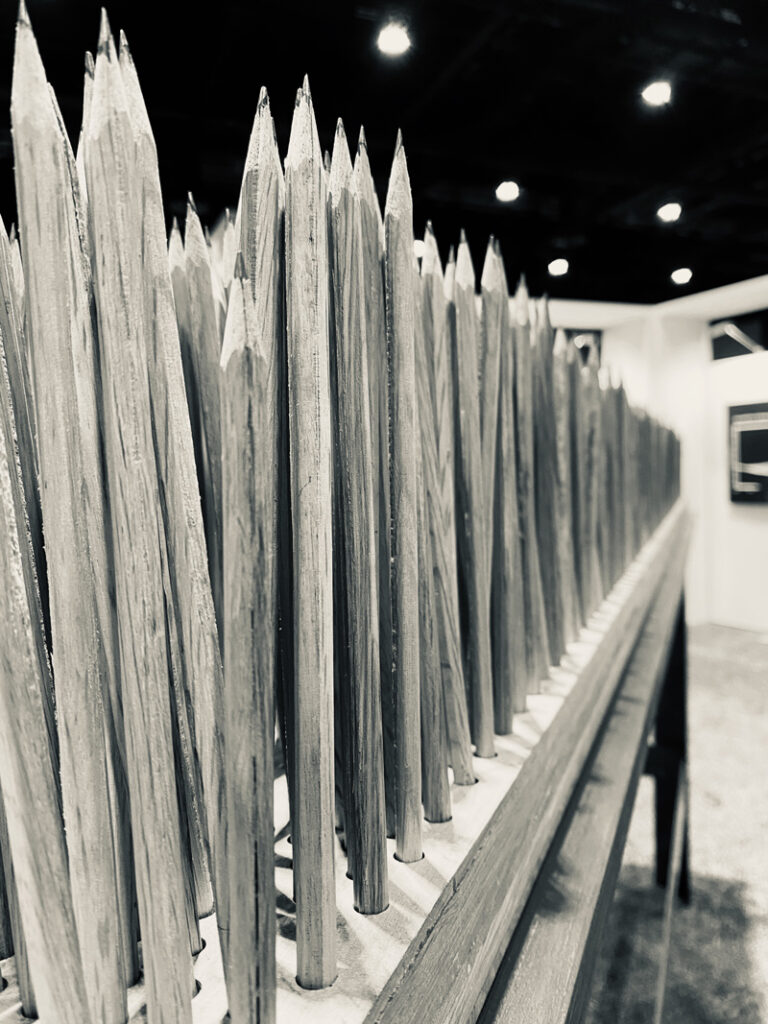 Black and white close-up view of a sculpture comprising numerous sharpened pencils standing vertically on a table