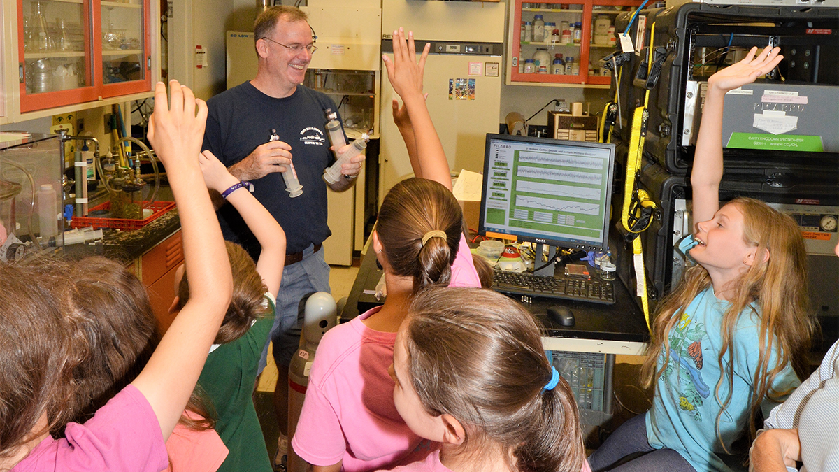 Photo of a scientist with a group of students in a lab.