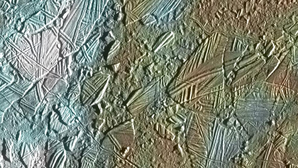 View of Jupiter’s moon Europa, with textured areas colored white, blue, tan, brown, and copper