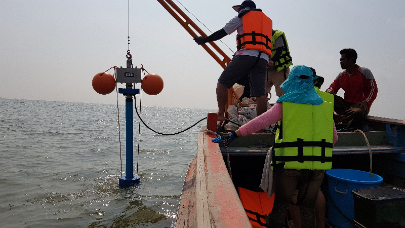 Four people on a boat operate a drilling device that pulls tubes of sediment from the seabed.