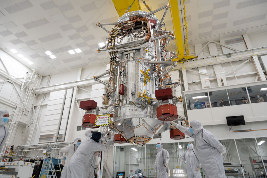 Engineers and technicians lift the tall core of NASA’s Europa Clipper spacecraft.