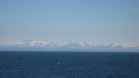 Photo of an ocean with snow-capped mountains in the background.