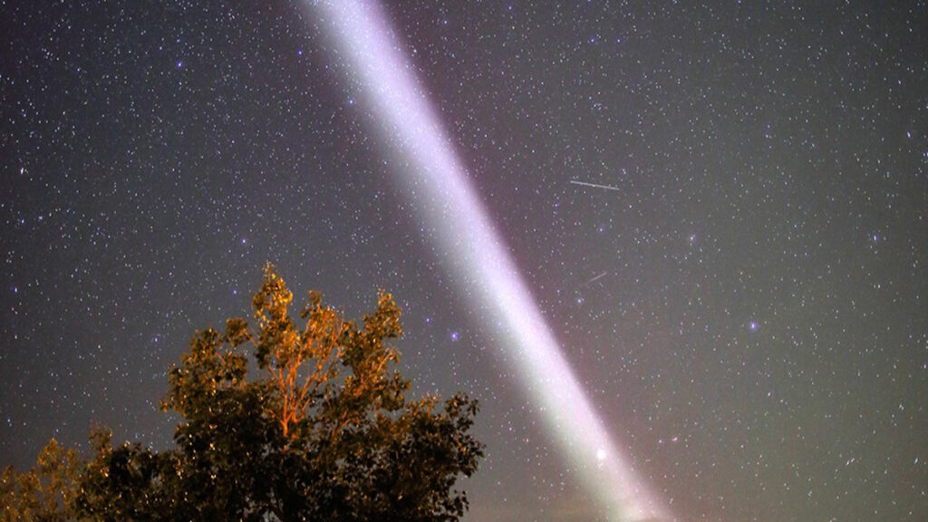 A bright ribbon of light stretches across a star-filled view of the night sky.