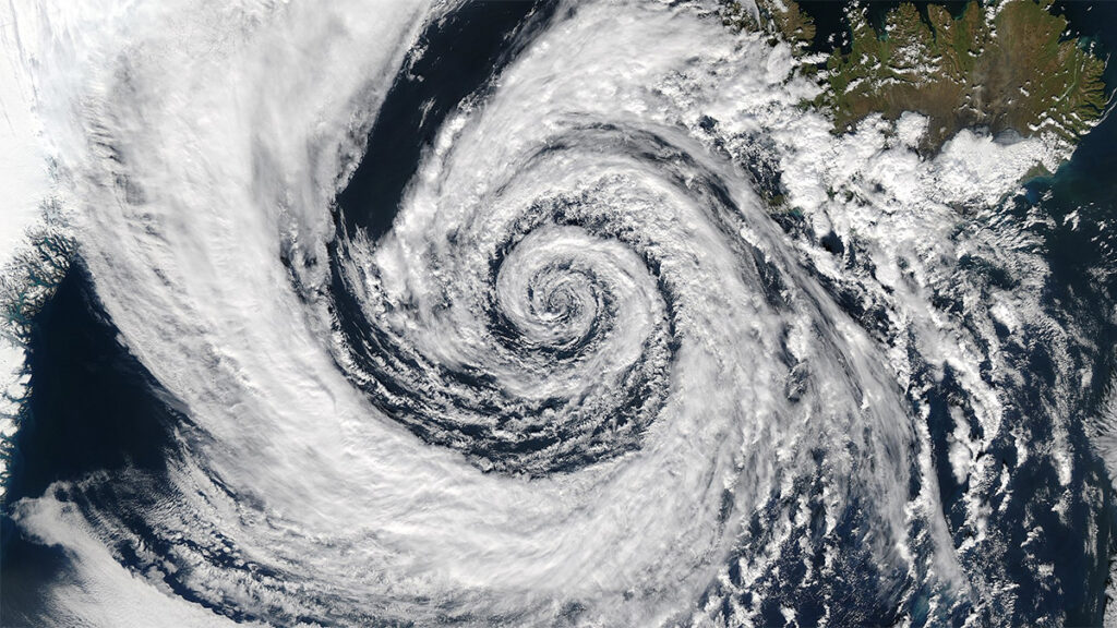 A spectroradiometer image of a low-pressure system of clouds off the southeastern coast of Iceland. The clouds have a cotton-like appearance and form a loose counterclockwise spiral.