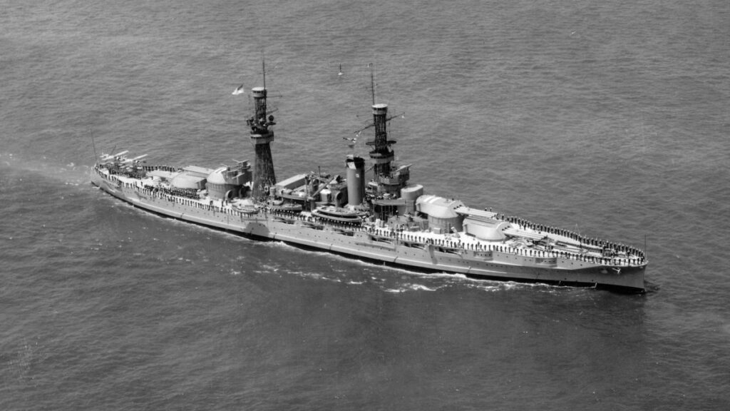 A black-and-white aerial photograph of an early 20th-century U.S. naval battleship on a calm sea.