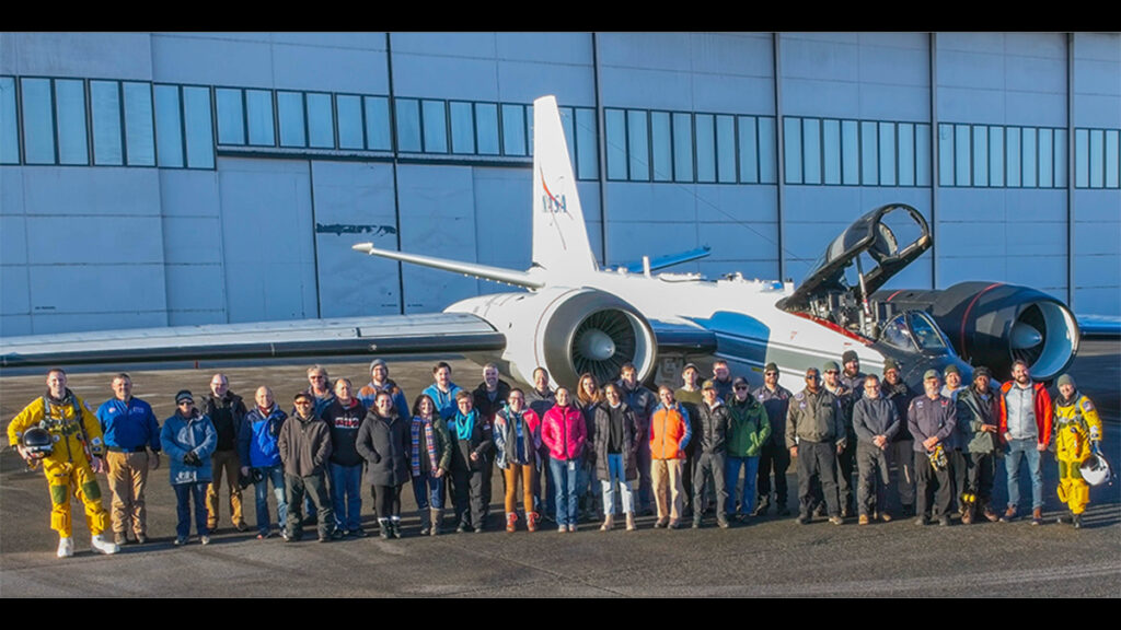 A line of people stand next to a plane.