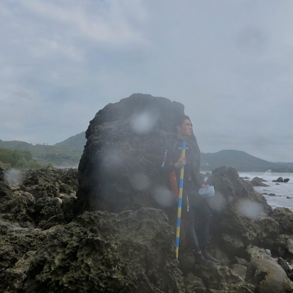 A researcher stands next to a coral boulder as tall as he is.