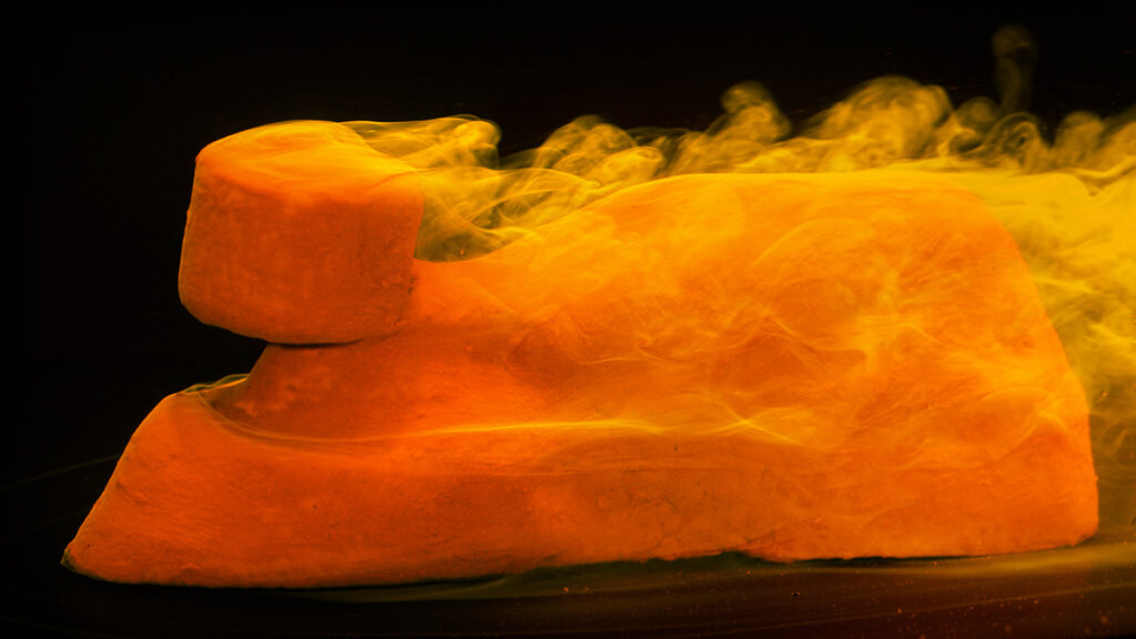 A mound of clay in a flow tunnel is eroded by water.