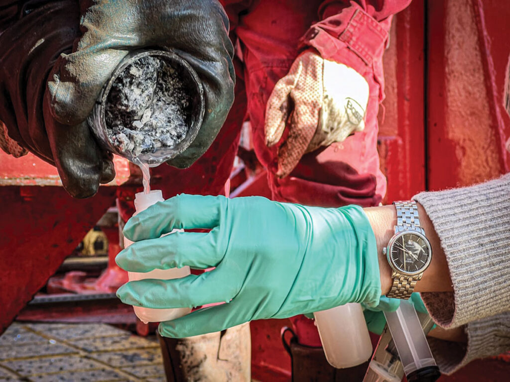 The gloved hands of Susan Lang pour fluid from a pipe into a plastic container.