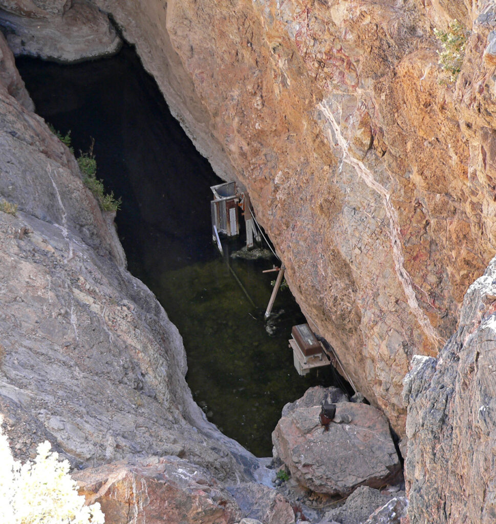 A rectangular pool of dark water below tall cliffs