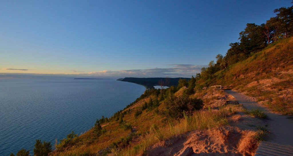 A wooden boardwalk leads along a bluff toward a rocky outcrop that extends over water.