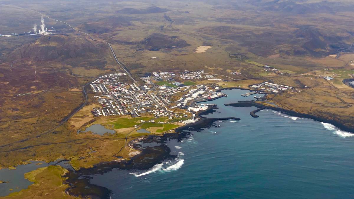 Image of a coastal town seen from the air with a geothermal power plant in the background.