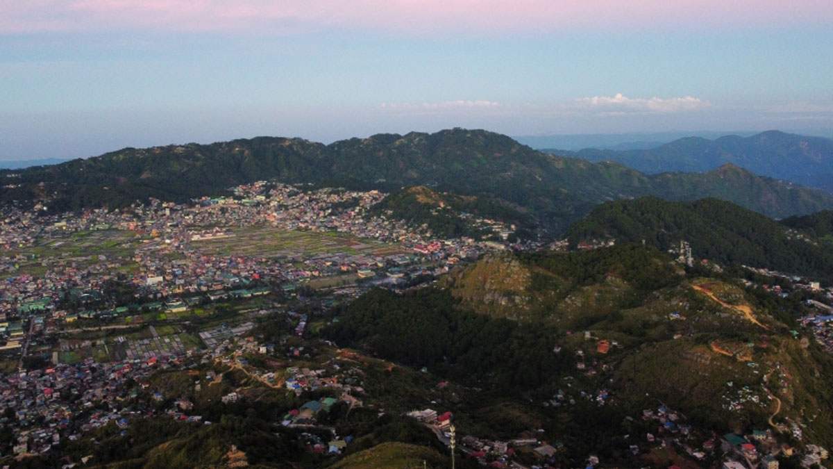 A drone shot of the Philippines’ Cordillera Central mountain range. The tops of the mountains are green with forest, but much of the land has been cleared and covered with buildings.