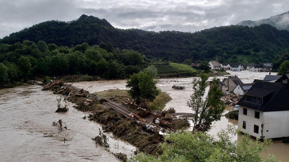 A brown river overflows its banks in a green, hilly region with houses.