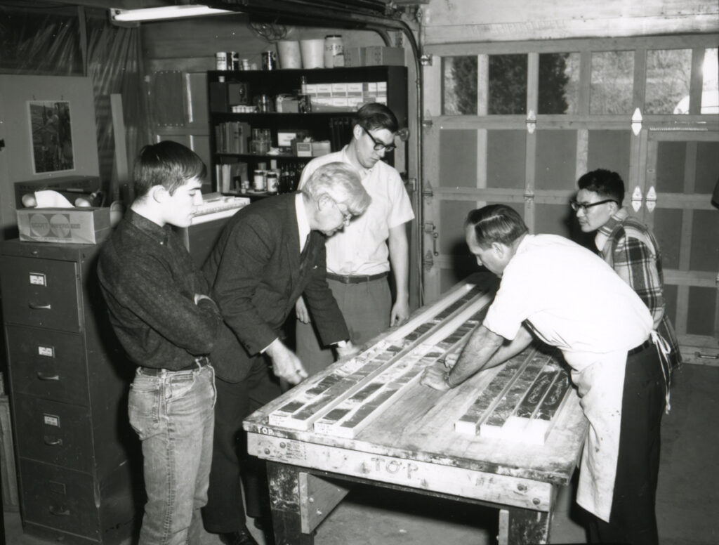 Black-and-white image of five people standing around a table studying sediment core sections inside a lab