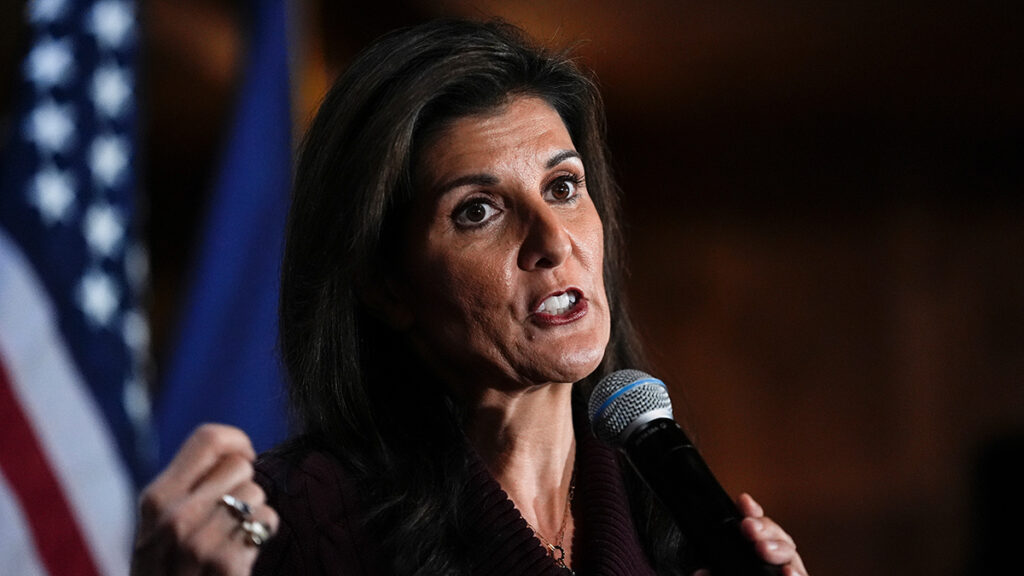 Nikki Haley holds a microphone in front of an American flag.