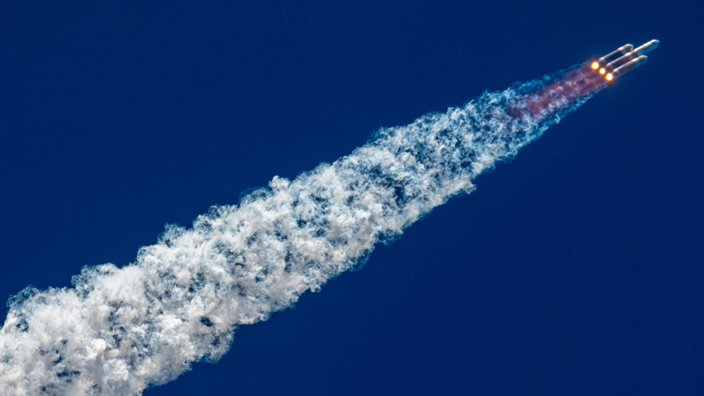 A rocket streaks across a dark blue sky, from the bottom left to the top right, leaving behind a bright white contrail.