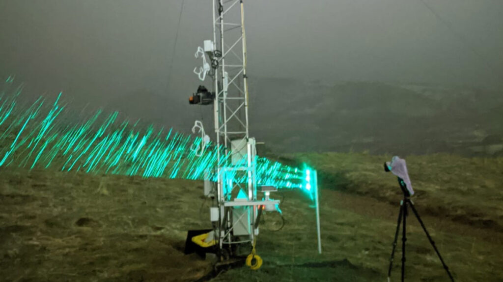 Green laser lights across a hillside used to capture falling snowflakes.