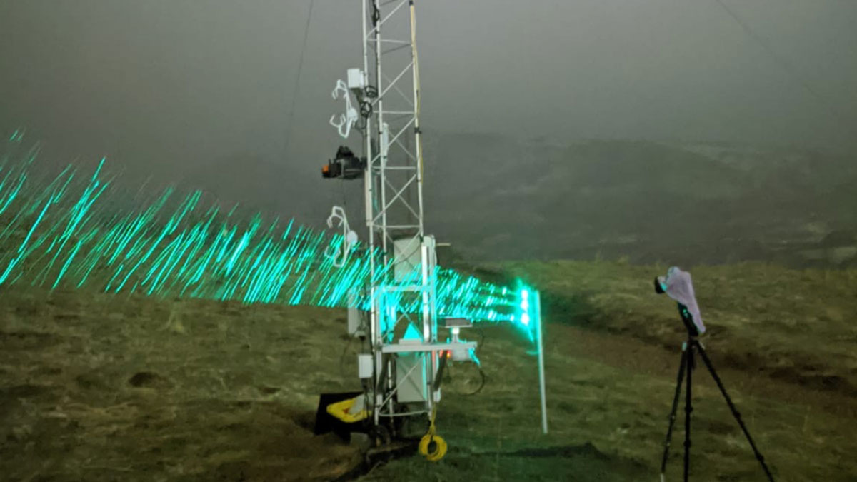 Green laser lights across a hillside used to capture falling snowflakes.