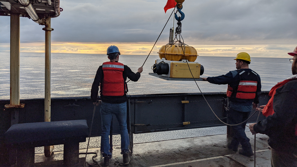 Scientists on a boat lowering a seismometer into the water.