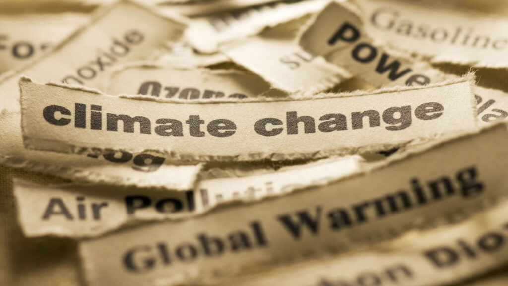 A small, rectangular piece of paper with the text “climate change” on it sits atop similar bits of paper bearing text such as “global warming” and “air pollution.”