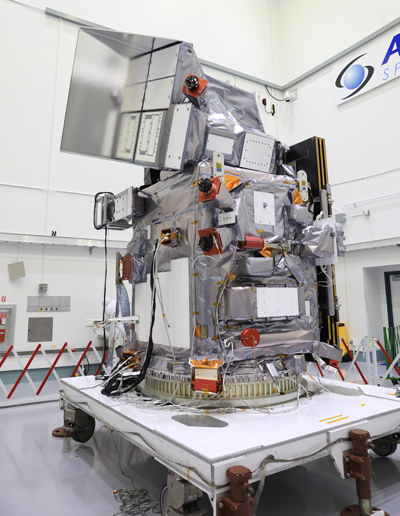 A gray metal spacecraft sits in a white room.