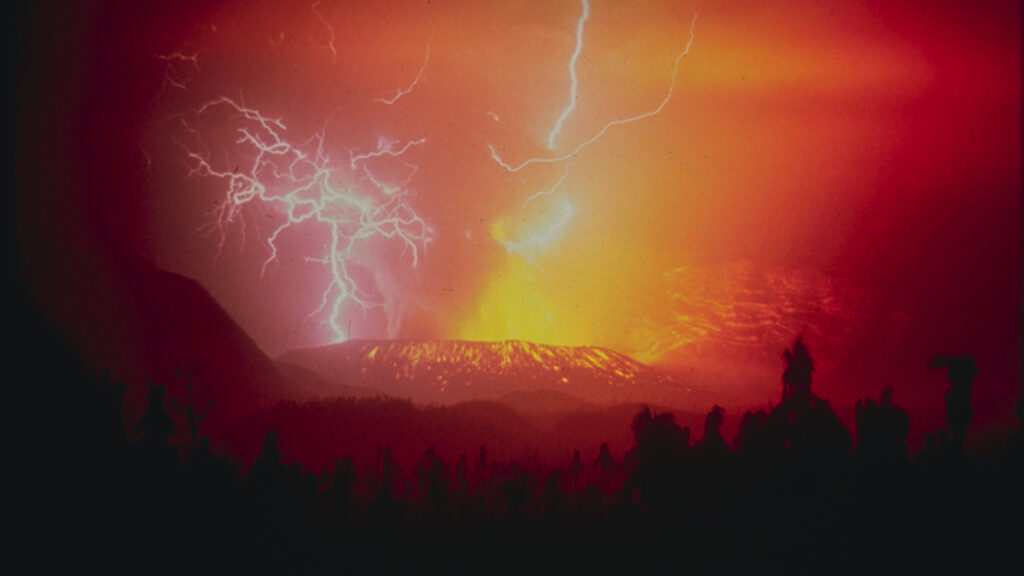 Lava and ash spewing from a volcano at night with several branching streaks of lightning.