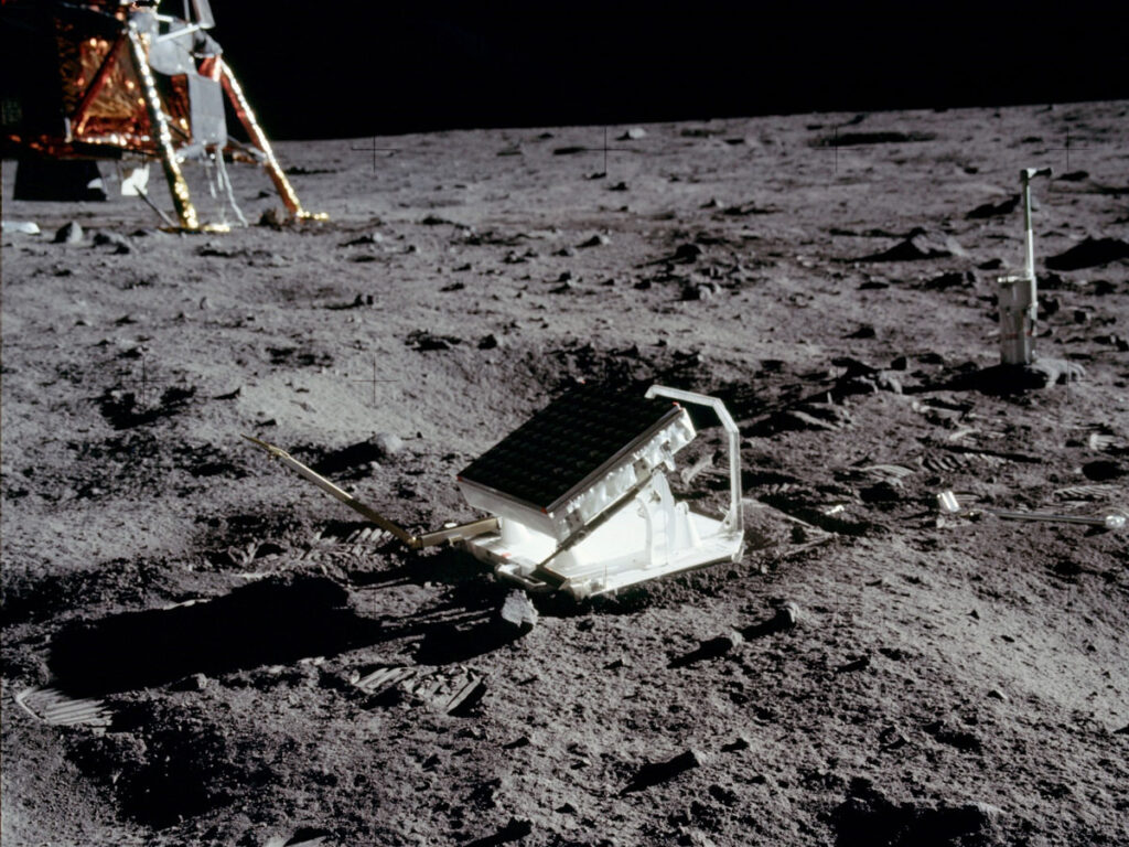 A small angled box rests on the Moon, with the Apollo Lunar Module in the background.