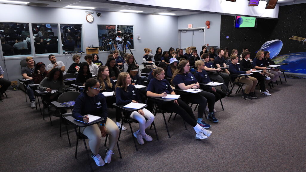 Students sit, writing on notebooks, in a classroom.