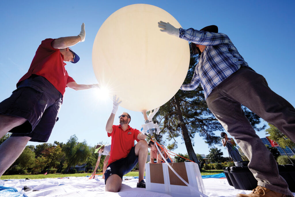 Three people are standing outside holding a white balloon roughly 1 meter in diameter.