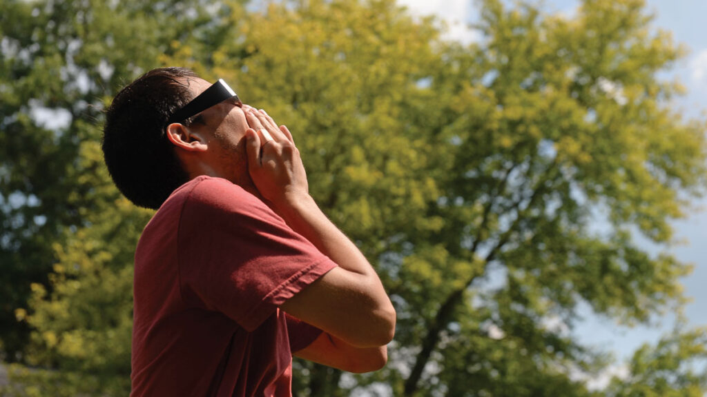 A man reacts while looking into the sun using solar eclipse glasses.